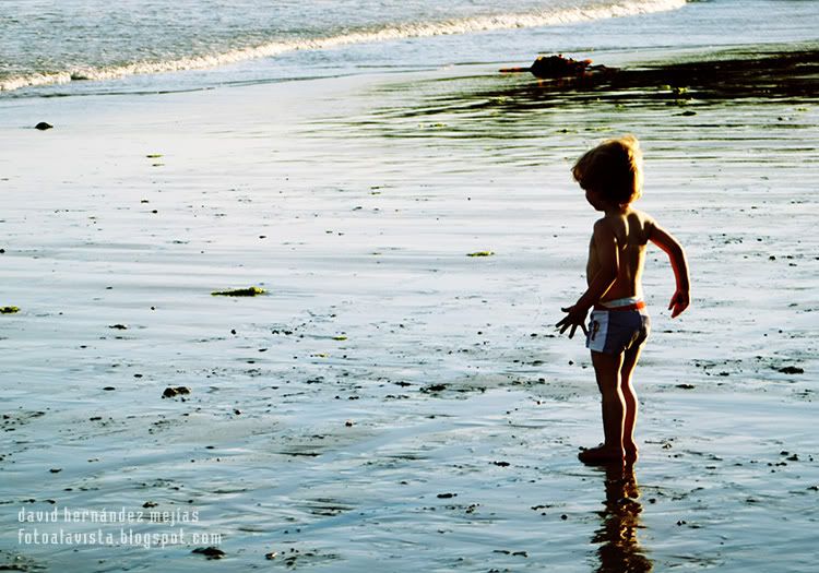 Niño reflejado sobre la arena mojada de la playa en la orilla del mar jugando con su pelota, en O Grove, Pontevedra, Galicia Ni me acerco al agua que está muy fría