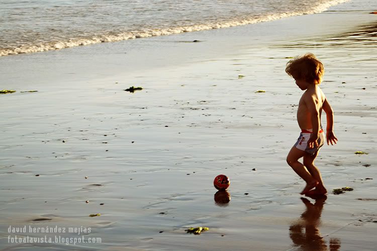 Niño reflejado sobre la arena mojada de la playa en la orilla del mar jugando con su pelota, en O Grove, Pontevedra, Galicia Niño y su reflejo con pelota