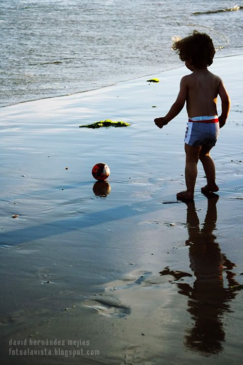 Niño reflejado sobre la arena mojada de la playa en la orilla del mar jugando con su pelota que se la lleva el viento hacia el interior, en O Grove, Pontevedra, Galicia Vino el viento y se la llevó
