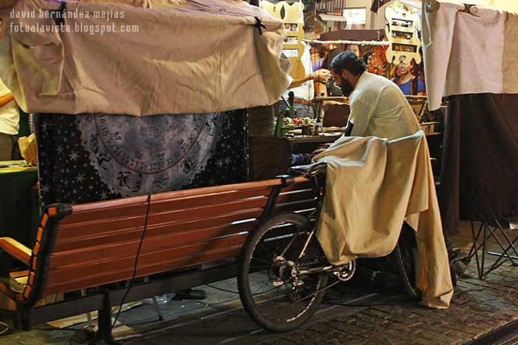 Un vendedor de un puesto de mercadillo ambulante medieval situado por detras del mostrador y por la perspectiva, se me asemeja un centauro acoplado a la bicicleta del primer término, en Majadahonda, Madrid El centauro nocturno